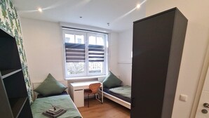 A compact room with two beds, a desk, and a chair. - Apartment Ilz - in the center, parking, kitchen, quiet location (Passau)