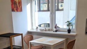 A dining area with a white table and wicker chairs, a wooden shelf unit, and a window with a view of the outside. - Apartment Ilz - in the center, parking, kitchen, quiet location (Passau)