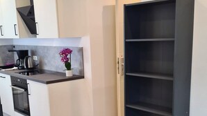 A modern kitchen with white cabinets, a black countertop, and a built-in oven. A black shelving unit is next to a bed with a green blanket. - Apartment Ilz - in the center, parking, kitchen, quiet location (Passau)