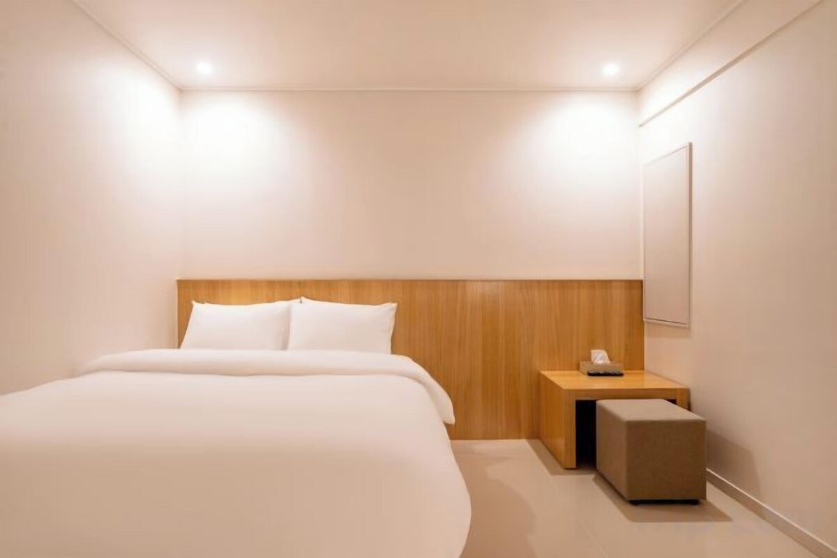 Une chambre d’hôtel moderne avec un grand lit, une tête de lit en bois, une table de chevet avec une lampe et une petite table de chevet avec un téléphone.