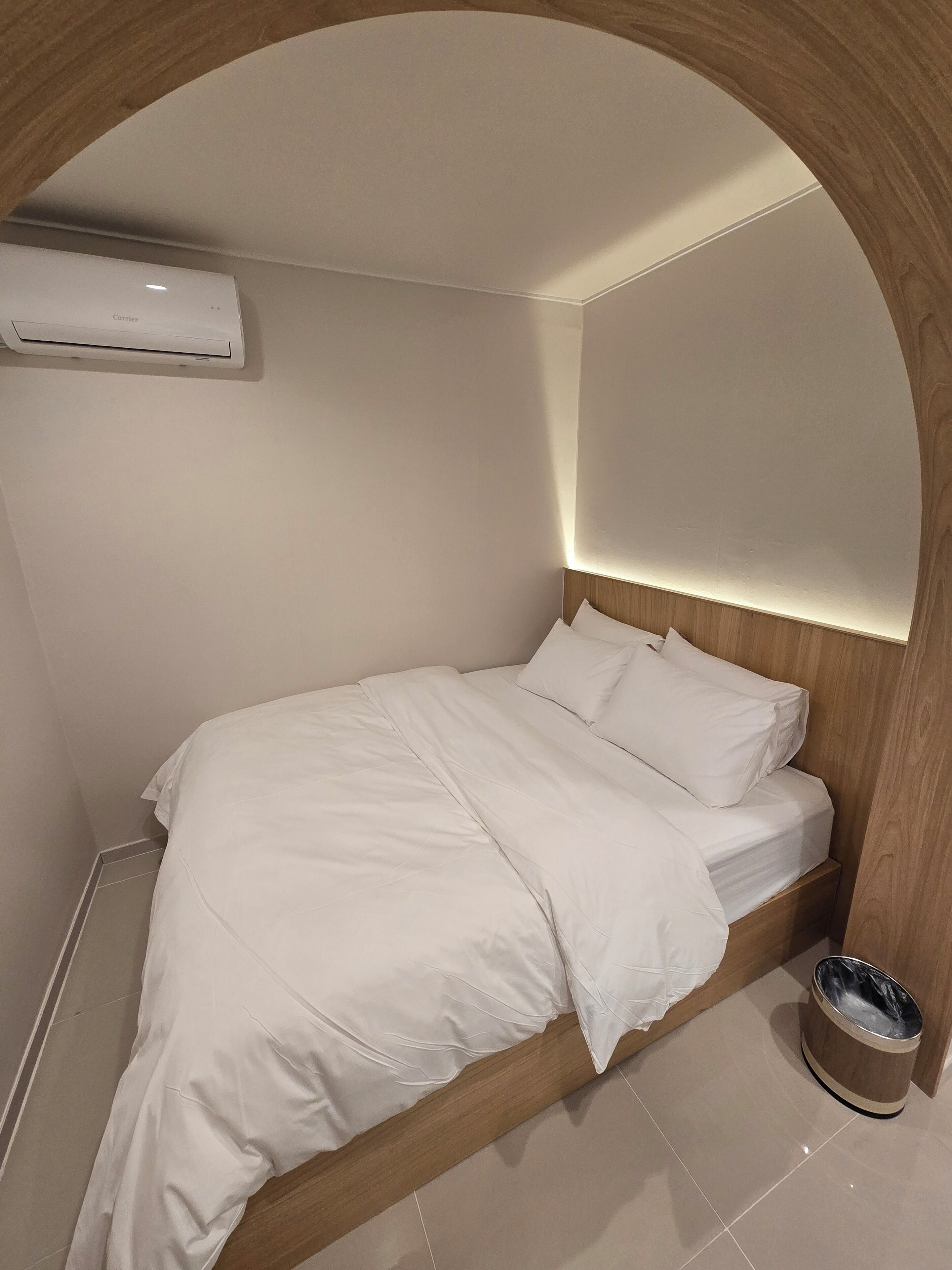 A neatly made bed with white linens in a room with a wooden headboard and a built-in air conditioning unit.
