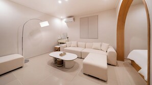 Un dormitorio moderno y minimalista con una cama grande, un sofá, una mesita y una lámpara de pie.