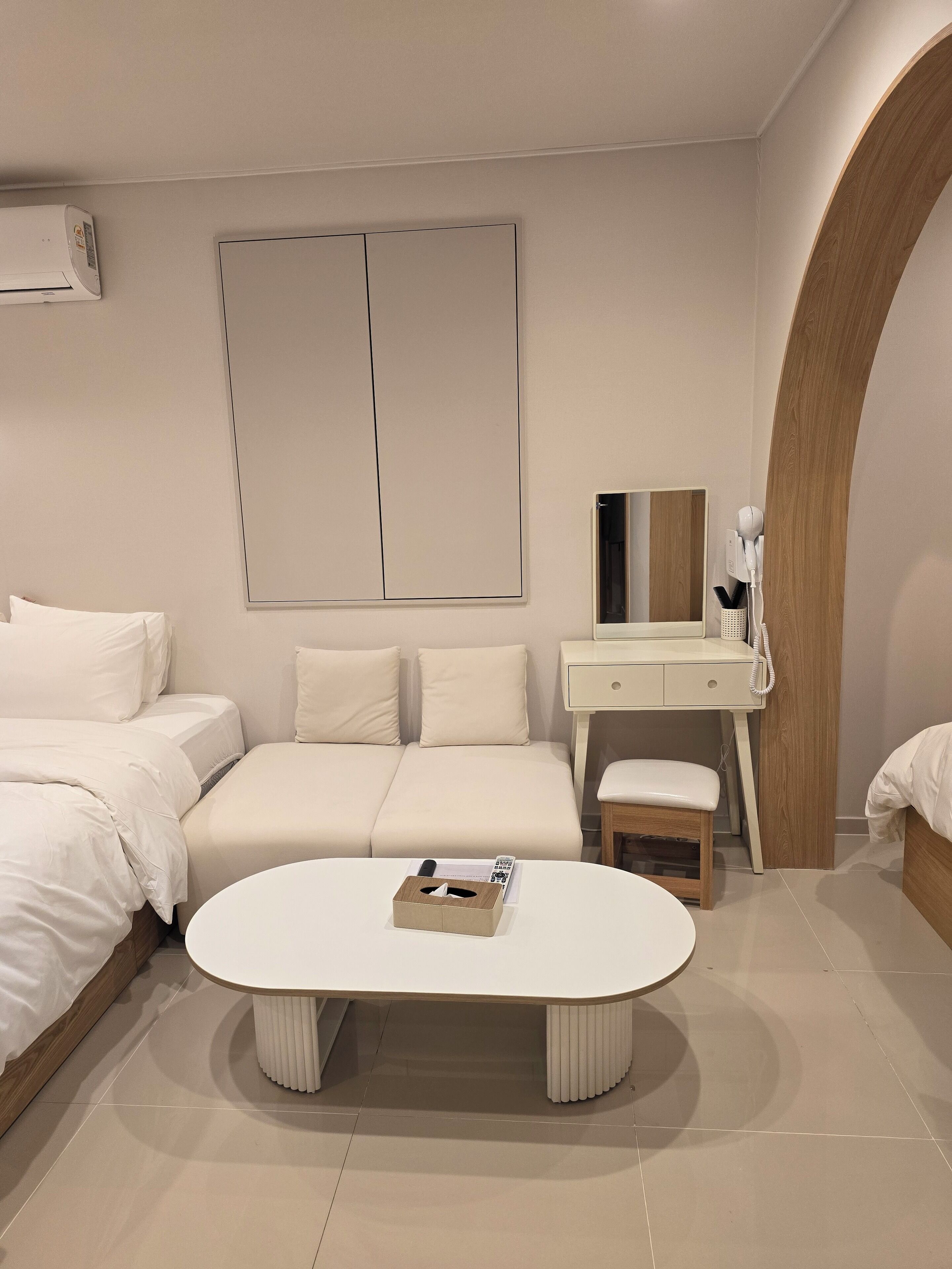 A modern bedroom with a bed, a sofa, a bedside table, a mirror, and a round coffee table.