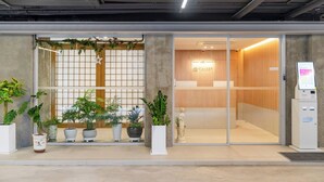 Entrada de un hotel con mostrador de recepción, quiosco de registro digital y plantas en macetas.