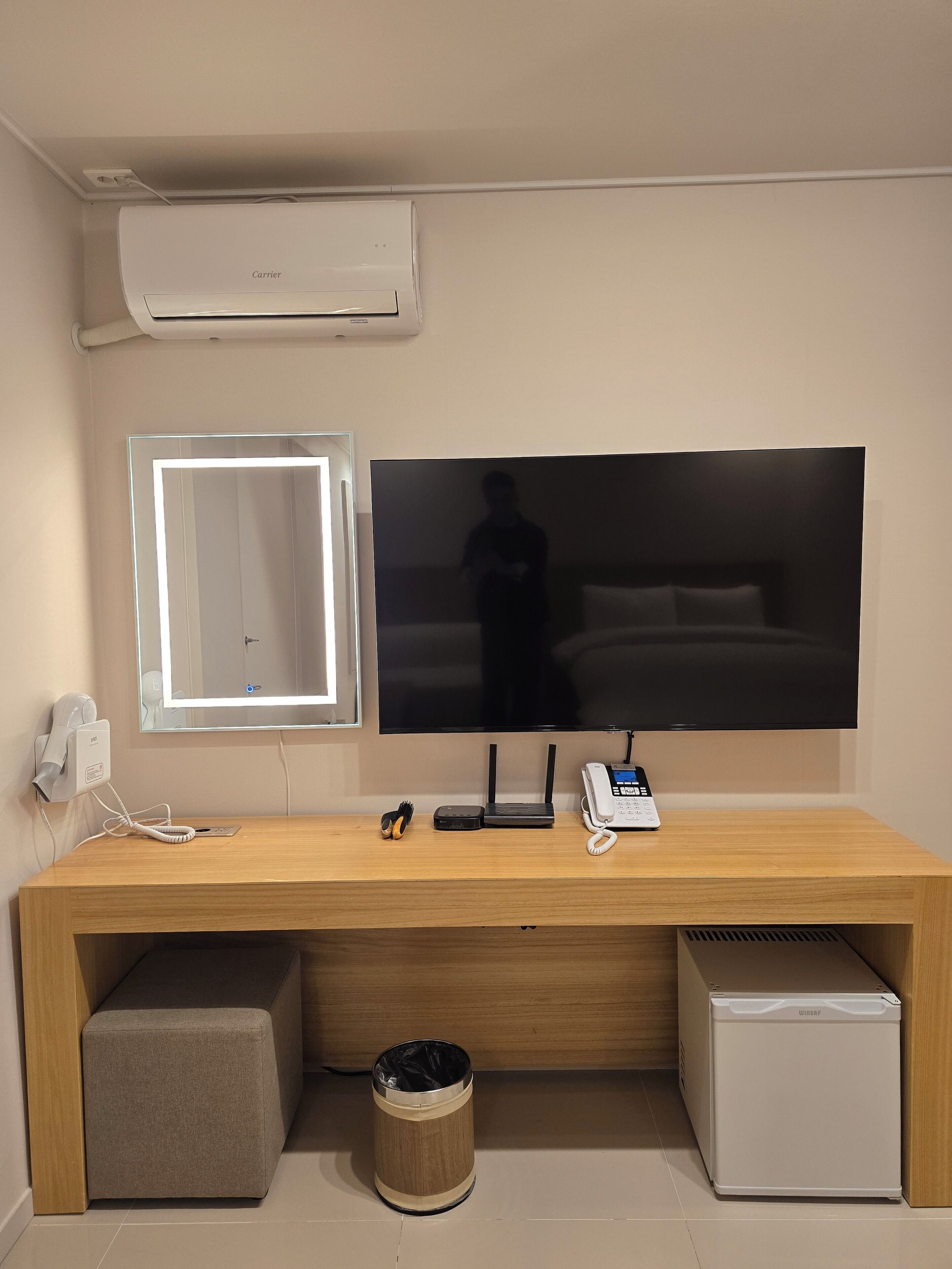 Un espacio de oficina moderno con una pantalla plana grande, un escritorio con computadora, teléfono y un refrigerador pequeño.