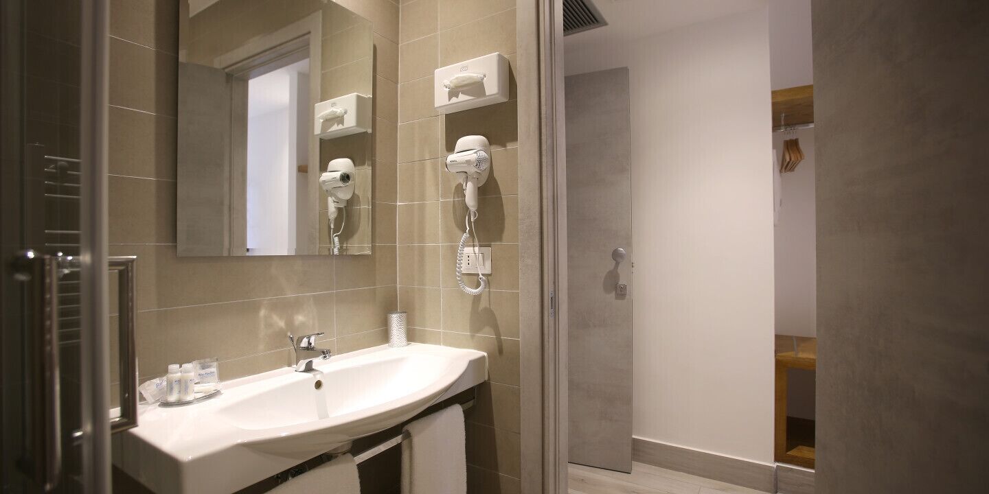 A modern bathroom with a sink, mirror, hairdryer, and towel rack.
