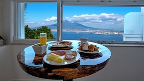 A breakfast table with plates of food and a glass of orange juice, overlooking a city and a mountain. - Relais Manfredi (Castellammare di Stabia)