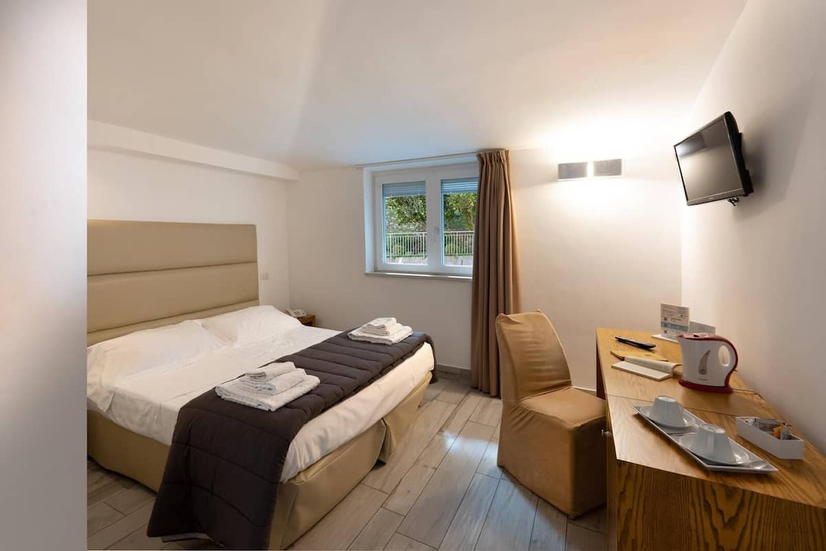 Habitación de hotel con cama, una silla, una mesa con tetera y televisor montado en la pared.