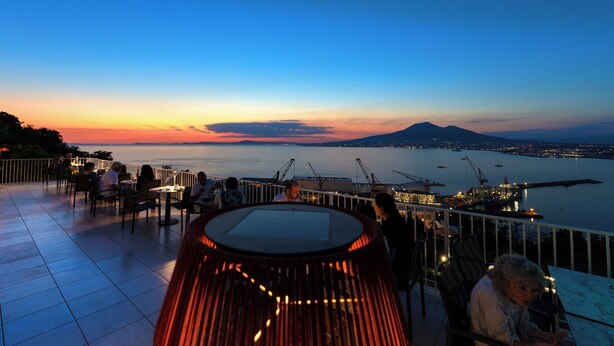 A terrace with tables and chairs overlooking a body of water at sunset. - Relais Manfredi (Castellammare di Stabia)