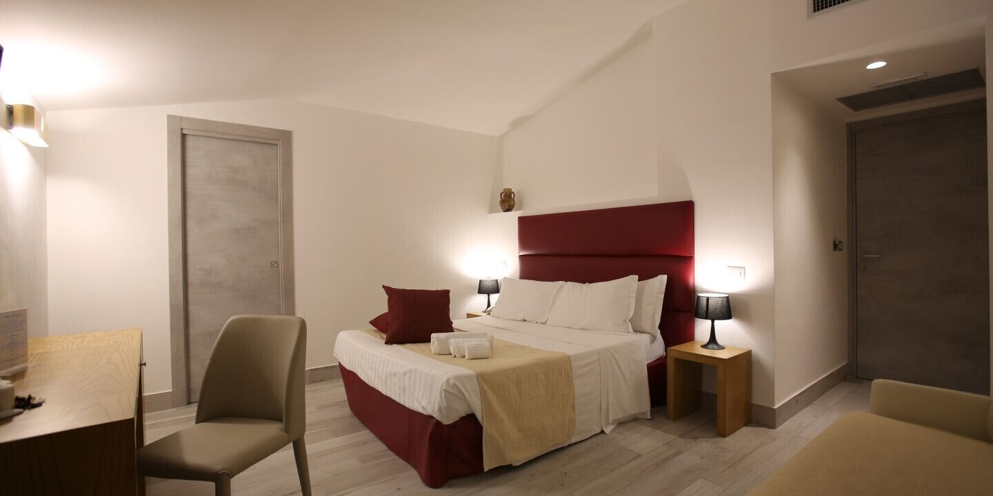 Ein Hotelzimmer mit einem Bett, zwei Nachttischen mit Lampen, einem Sessel, einem Schreibtisch und einem Kleiderschrank.