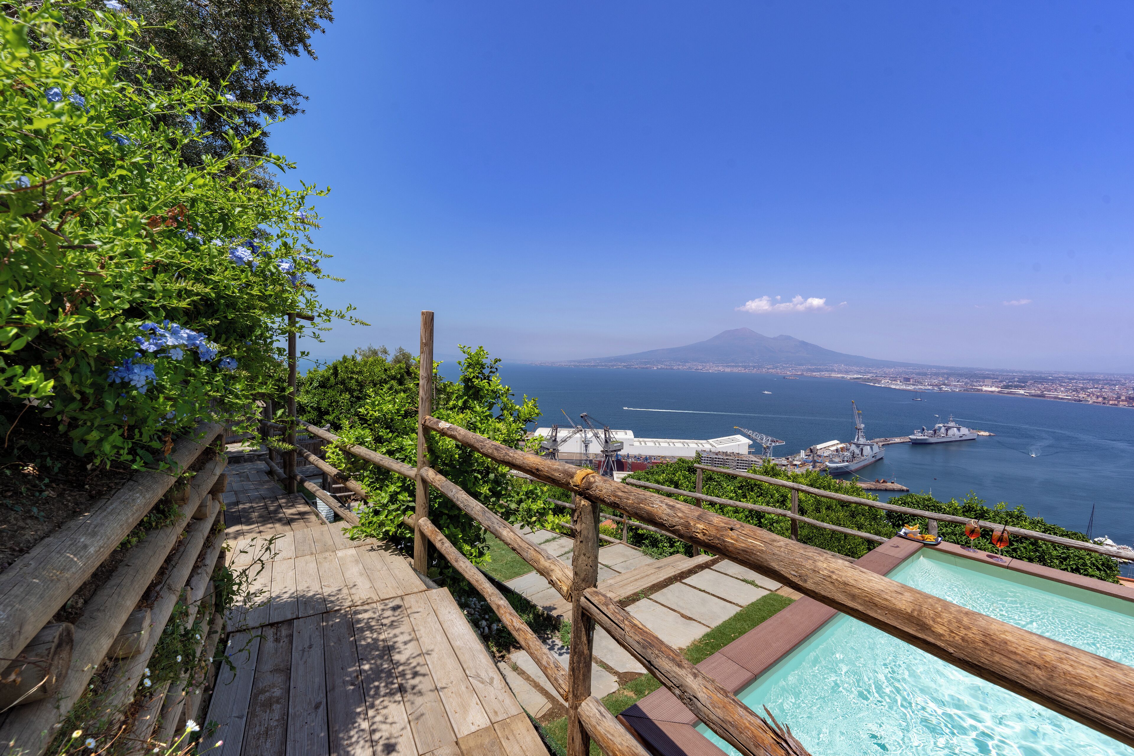 Una terraza de madera con piscina, con vistas a una ciudad costera y una montaña.