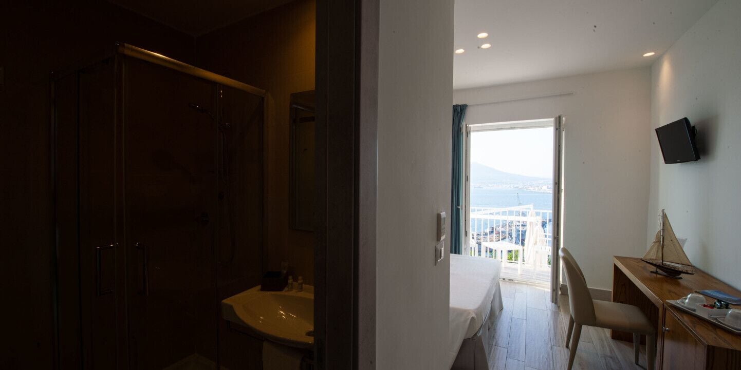 Een hotelkamer met een balkon, een bureau en een televisie.