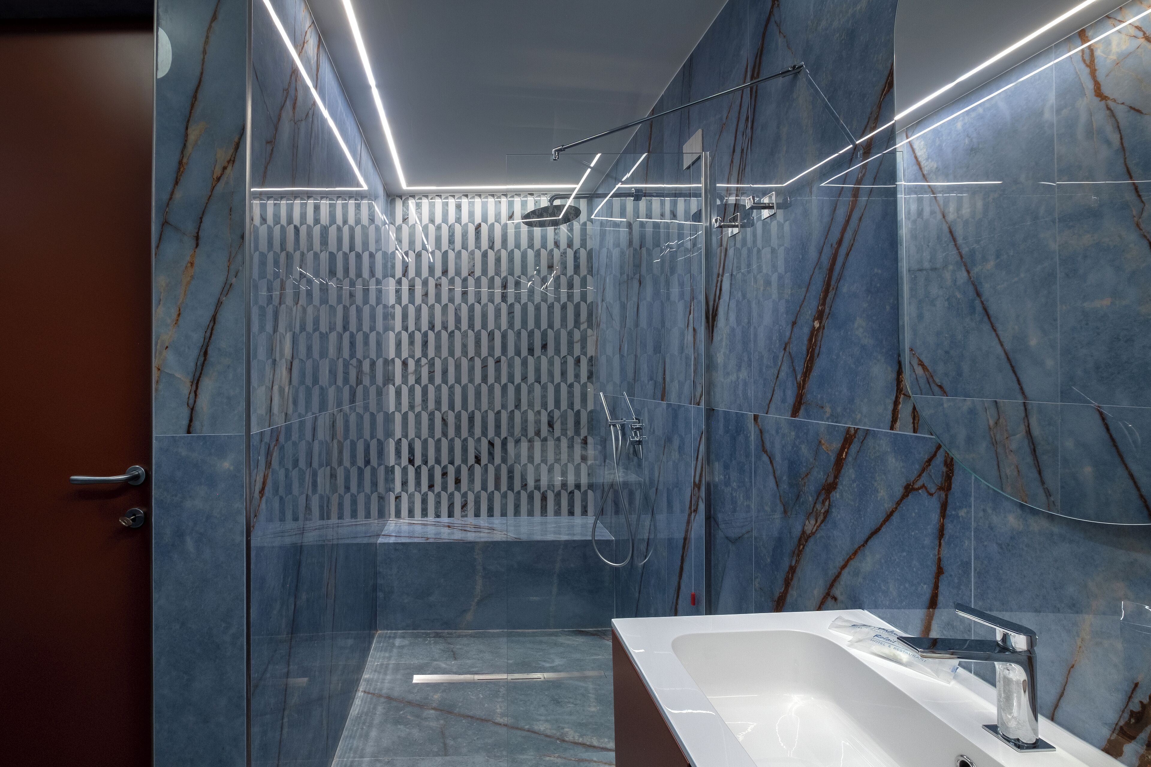 A modern bathroom with a glass shower enclosure, a white sink, and marble walls.