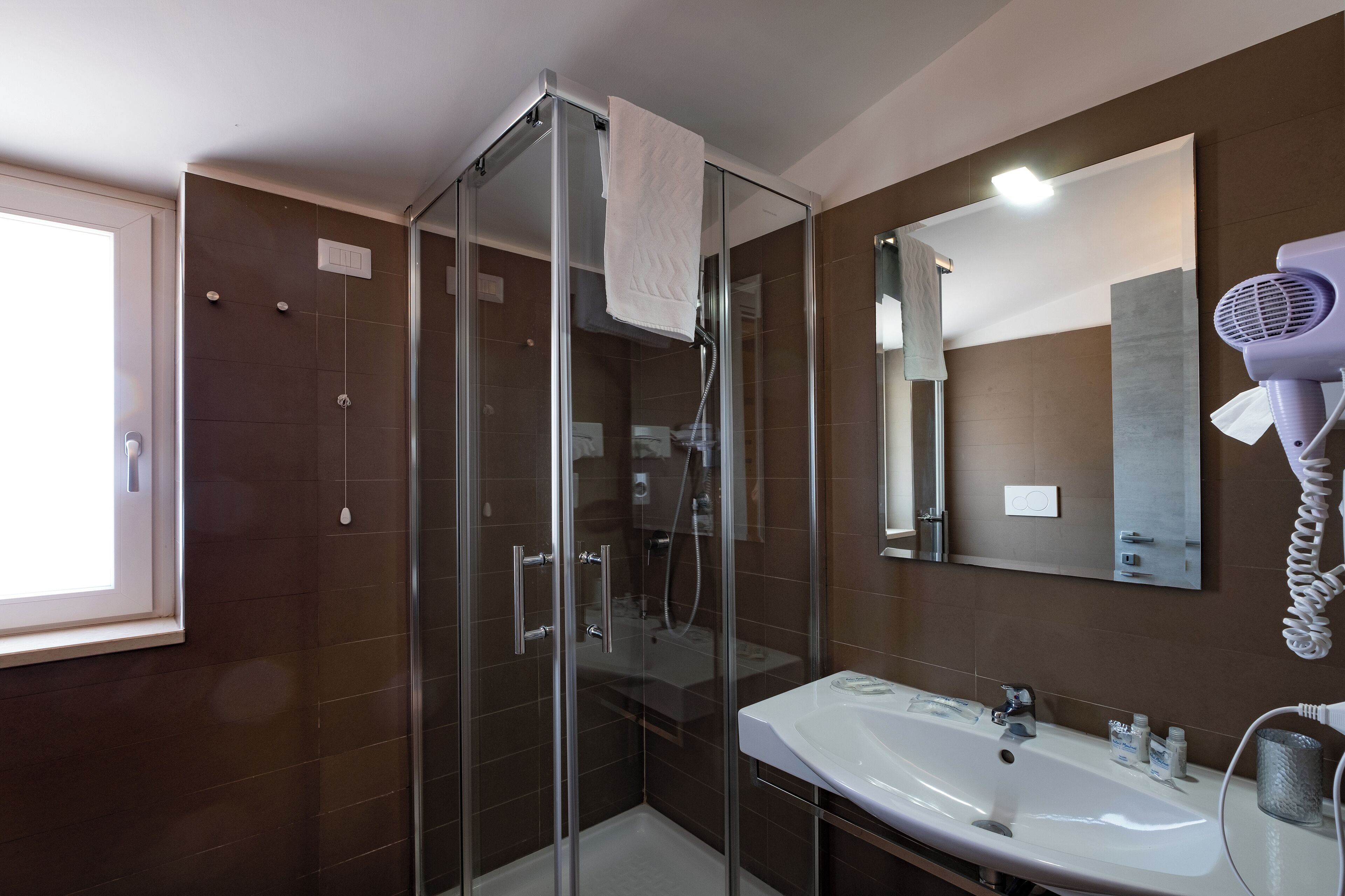 Un baño moderno con ducha envuelta en vidrio, un lavabo blanco y un secador de pelo en la pared.