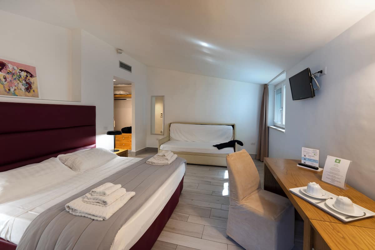 Habitación de hotel con una cama grande, un escritorio con silla, un televisor en la pared y una ventana.