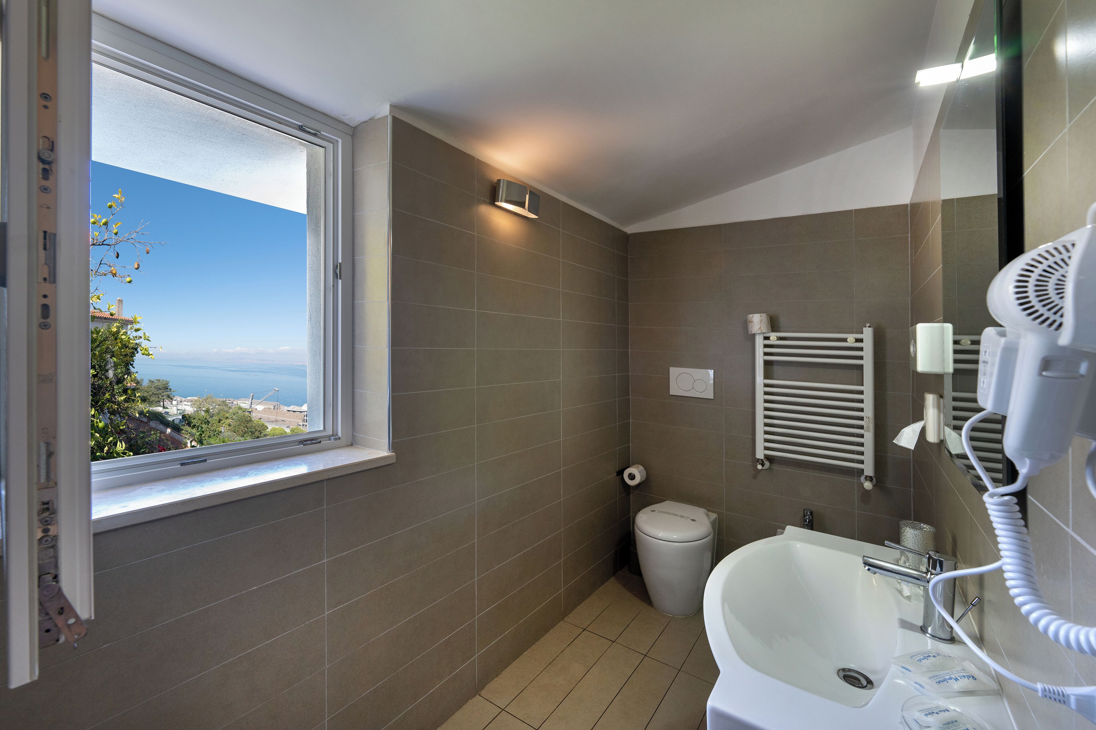Een badkamer met een raam, een wastafel, een toilet en een haardroger.