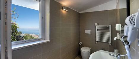 Ein Badezimmer mit Fenster, Waschbecken, Toilette und Föhn.