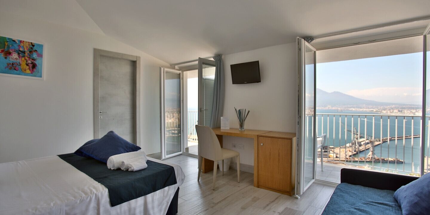 Habitación de hotel moderna con dos camas, un escritorio y un balcón amplio con vista a la ciudad y al agua.
