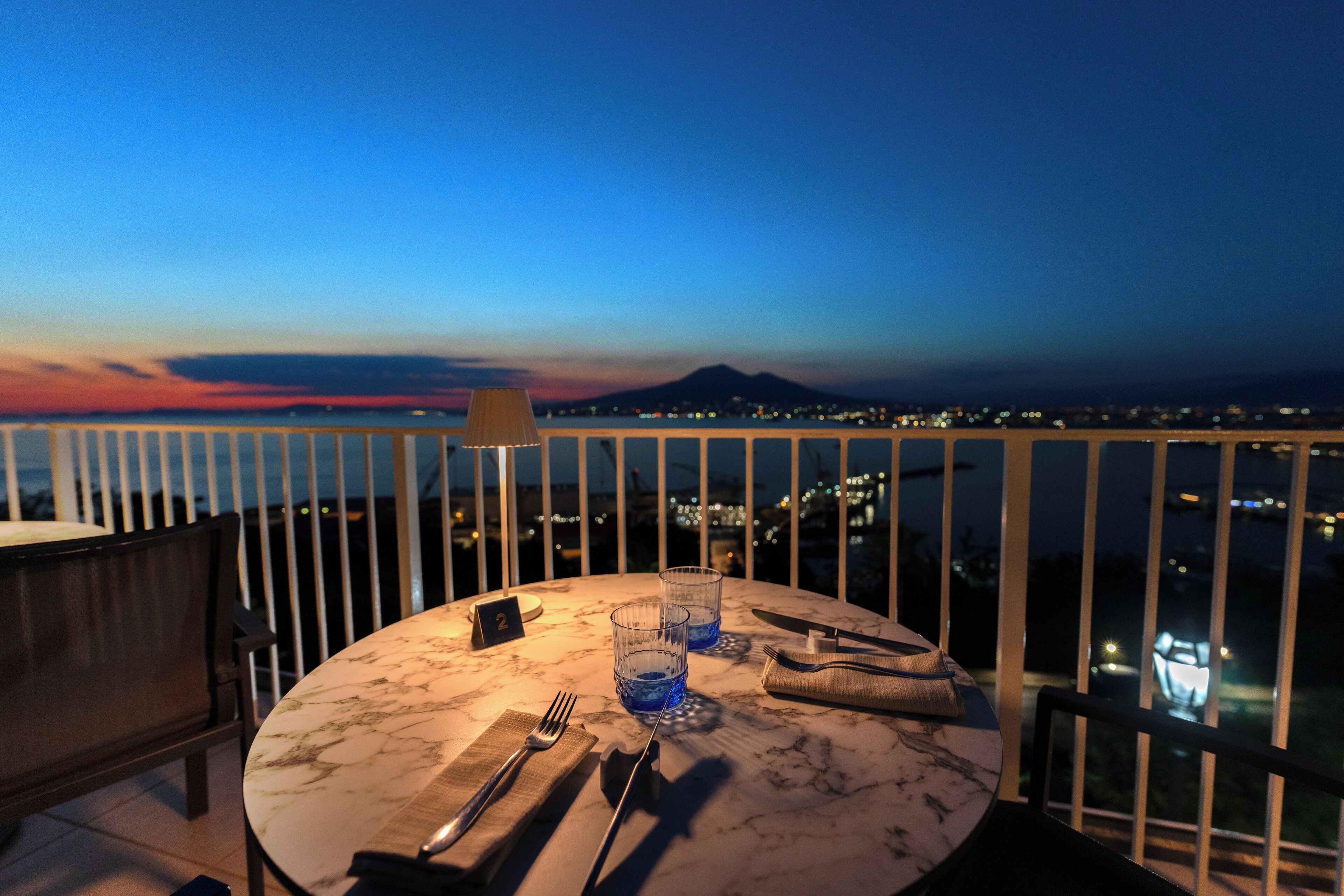 A table set for two with a view of a cityscape at dusk.