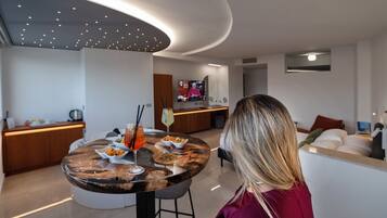 Uma sala de estar moderna com uma mesa de jantar redonda, um sofá e uma televisão ao fundo.