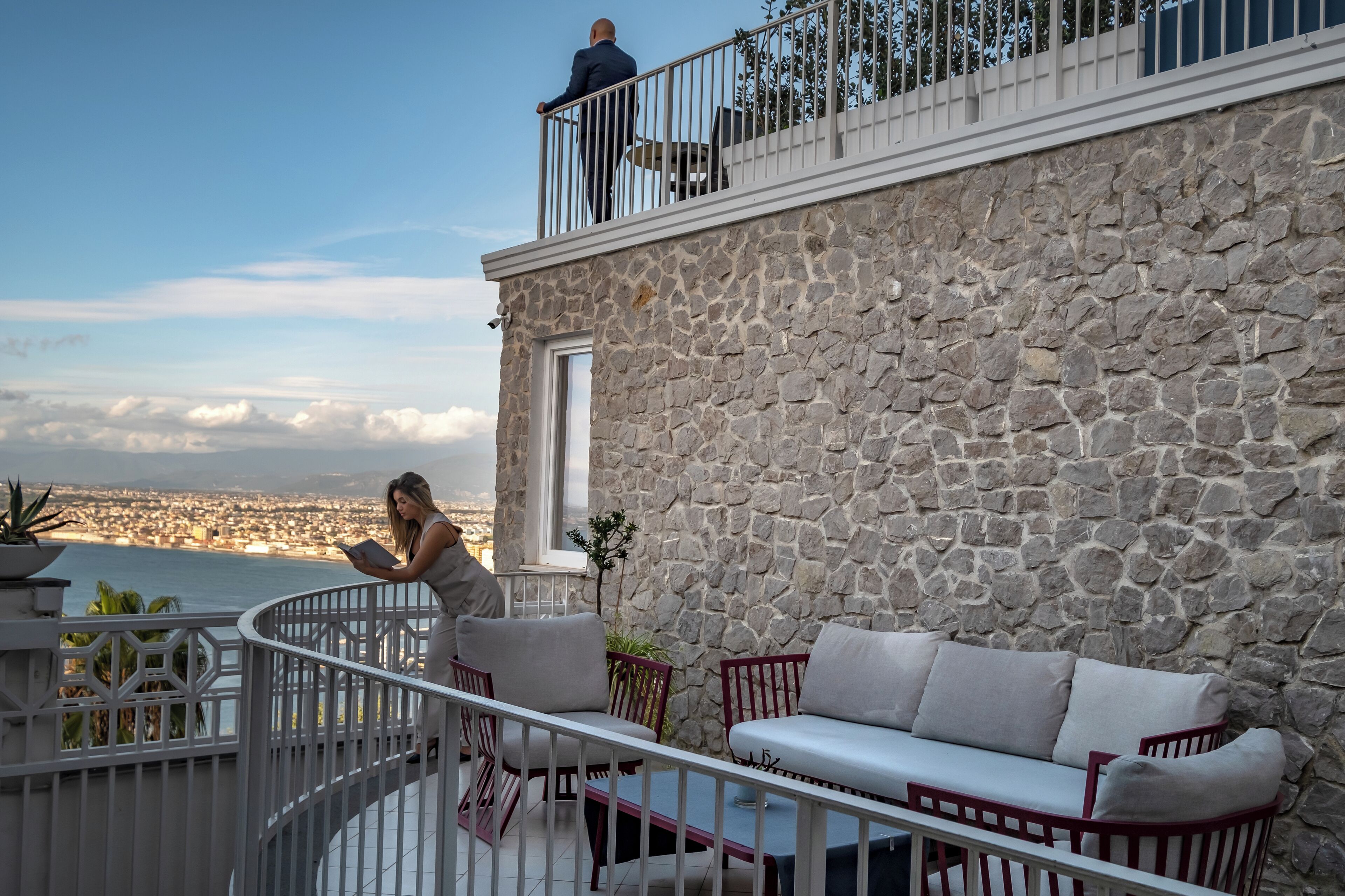 Un edificio de piedra con un balcón, barandilla blanca y vista panorámica de la ciudad.