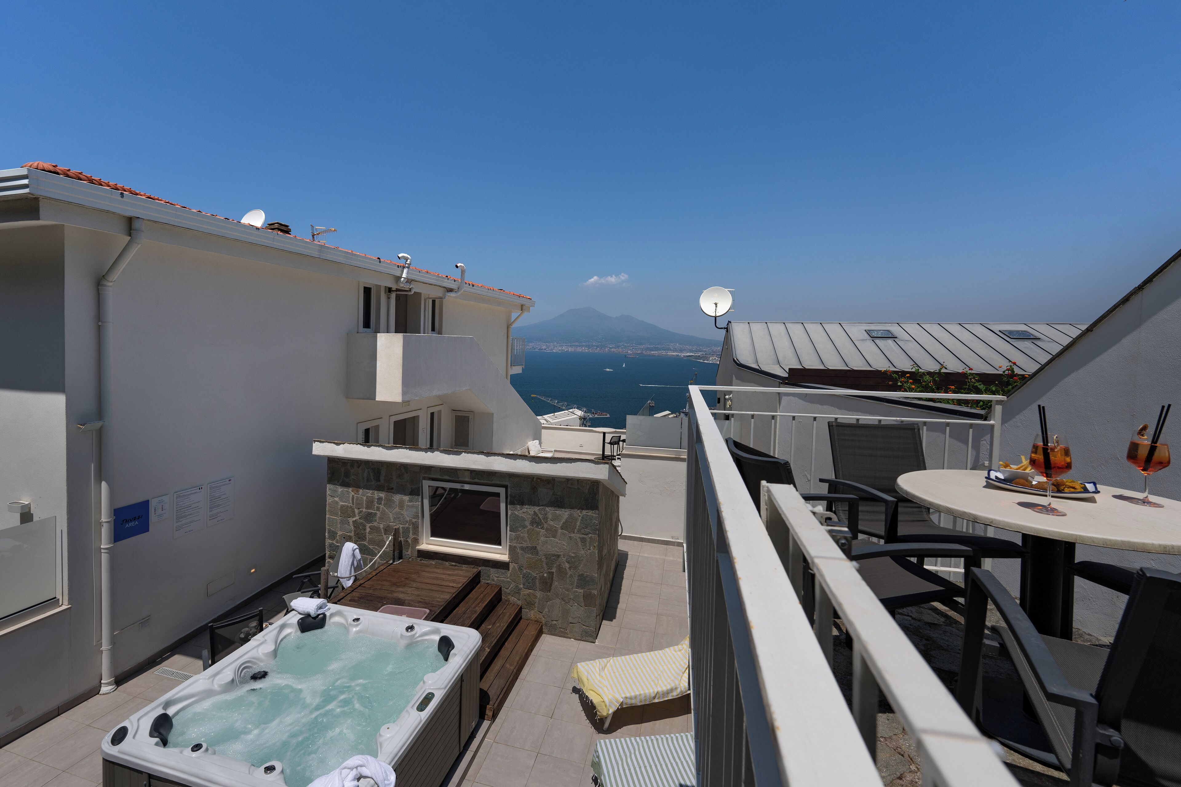 A rooftop terrace with a hot tub, outdoor seating, and a table with drinks.