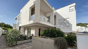 Un edificio moderno de dos pisos con un balcón, un espacio exterior cubierto y una entrada protegida por una reja.