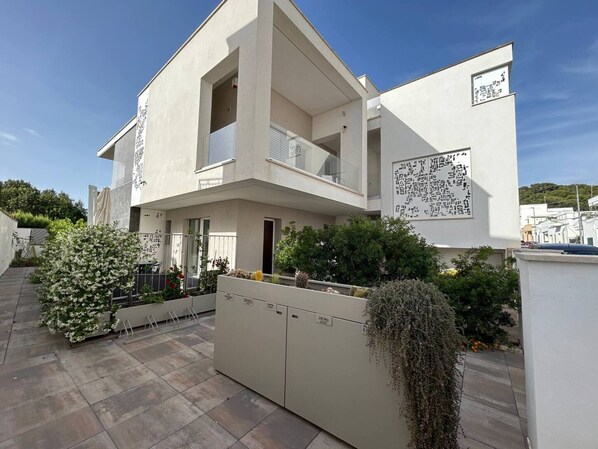 Un bâtiment moderne à deux étages, doté d’un balcon, d’un espace extérieur couvert et d’une entrée sécurisée par un portail.