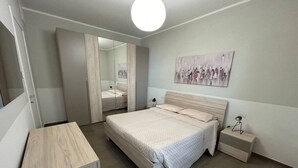 Un dormitorio con cama, mesita de noche, cómoda, espejo y un cuadro en la pared.