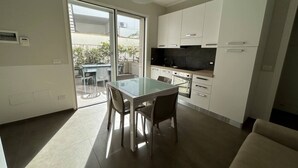 Una cocina moderna con armarios blancos, una mesa de comedor de vidrio y un ventanal corredero que da a un espacio exterior.