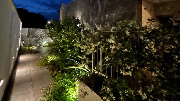 Un sendero lleva a un edificio con una sección superior iluminada en azul y un cartel con texto.