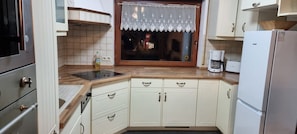 A compact kitchen with white cabinets, a built-in oven, a coffee maker, and a window with a lace curtain.