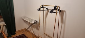 A room with a radiator, an ironing board, and a metal drying rack with hangers.
