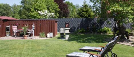 A backyard with two sun loungers, a barbecue grill, and a red barn.