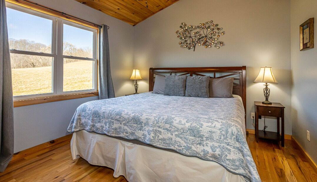 A bedroom with a bed, two bedside tables, a window, and a wall decoration.