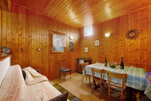 Een houten interieur met een bed, een eettafel met stoelen, een raam en wandlampen.