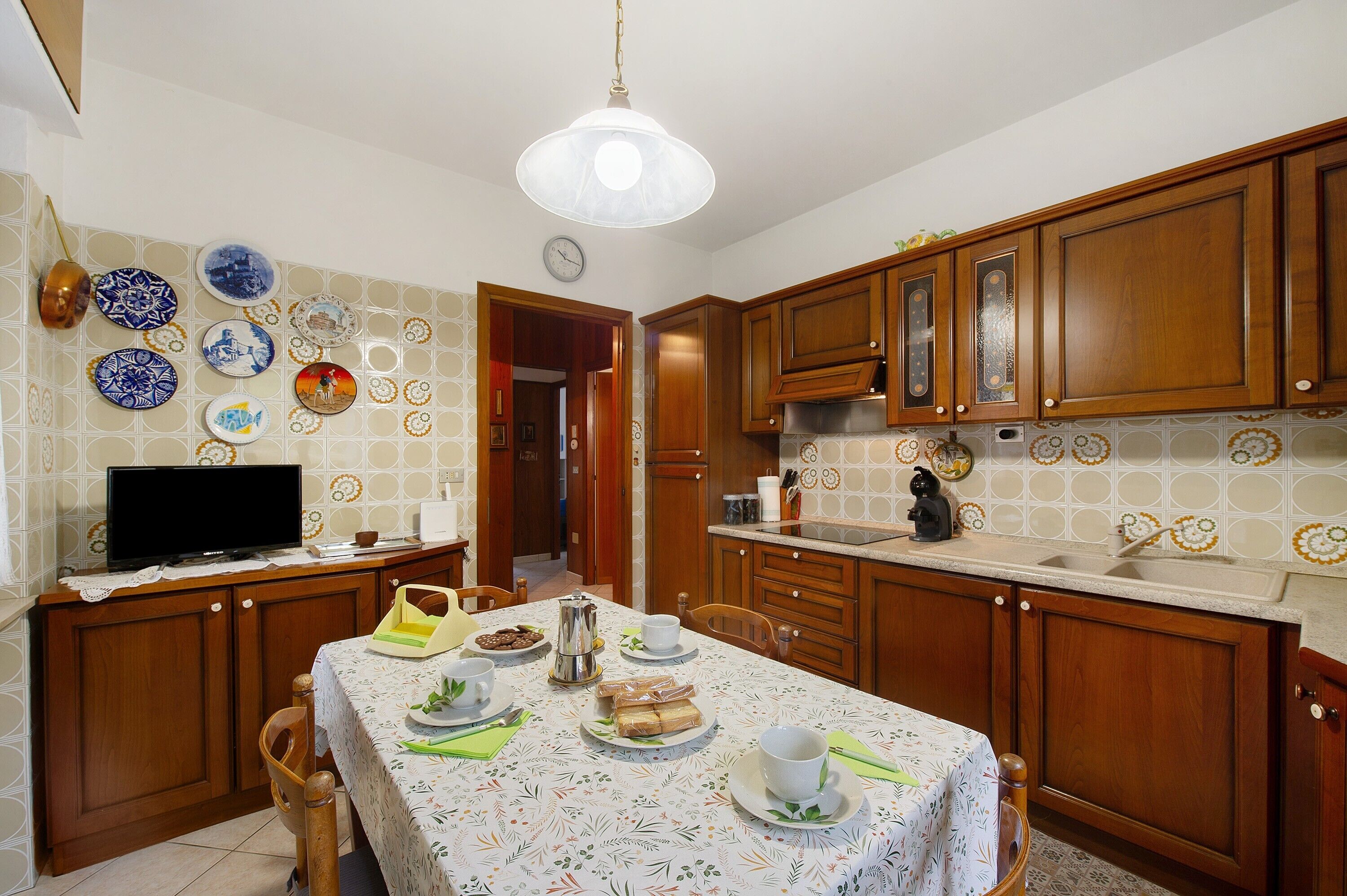 A kitchen with wooden cabinets, a dining table set with plates and cups, and a television on the counter.