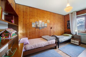 Een kamer met houten lambrisering, twee bedden, een plank met boeken en een raam met uitzicht.