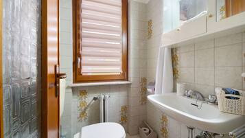 Ein Badezimmer mit Toilette, Waschbecken, Fenster und Duschbereich.