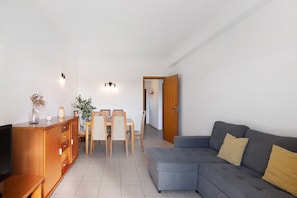 A living room with a sofa, TV, wooden cabinet, dining table, chairs, and a door leading to another room.