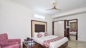 A hotel room with a bed, a chair, a bedside table with bottles, a ceiling fan, and a mirror. - Hotel New Palace (Dalhousie)