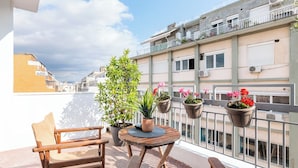 A balcony with a wooden table, two chairs, and potted plants.