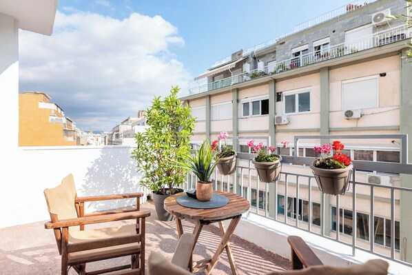 A balcony with a wooden table, two chairs, and potted plants. - Marabou Unique Stay (Thessaloniki)