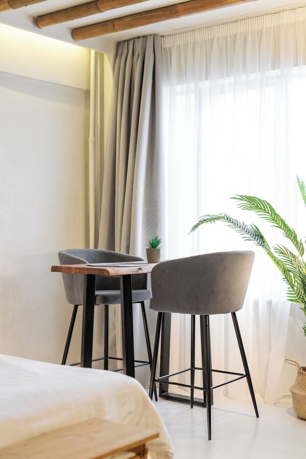 A modern hotel room with a bed, two grey chairs, a wooden table, and a potted plant. - Marabou Unique Stay (Thessaloniki)