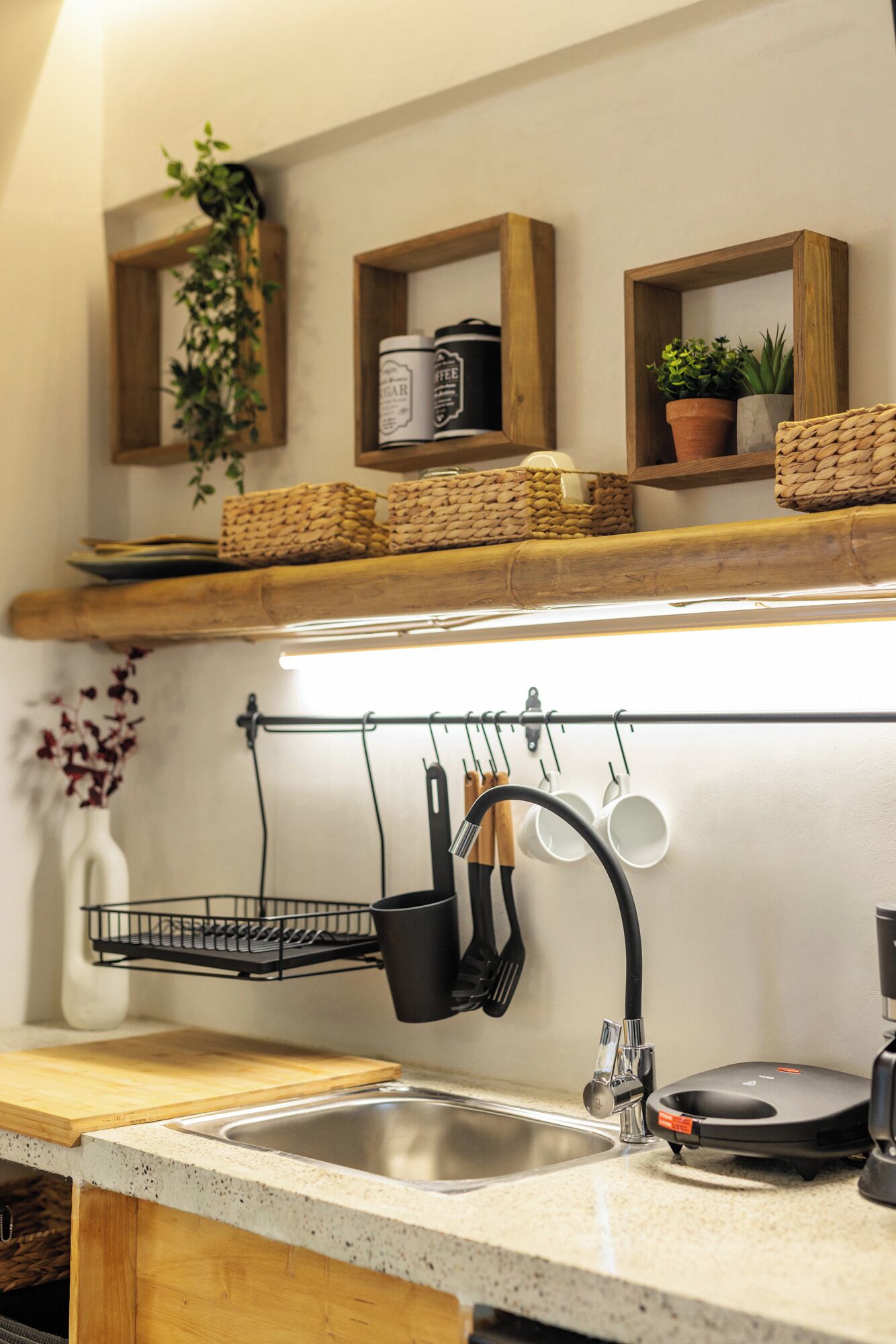 A kitchen with a stainless steel sink, wooden countertops, hanging utensils, and shelves with potted plants and kitchen items.