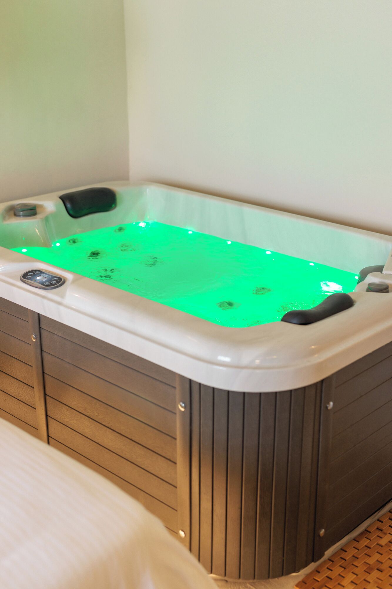 A hot tub with a green light, wooden paneling, and a control panel.