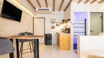 Una cocina moderna con encimera de madera, estufa integrada y un lavabo. Hay un televisor montado en la pared y una puerta que da a otra habitación.