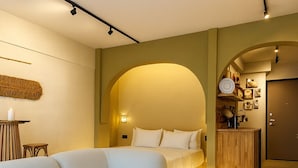 A modern bedroom with a large L-shaped sofa, a bedside table with candles, and a wooden cabinet.