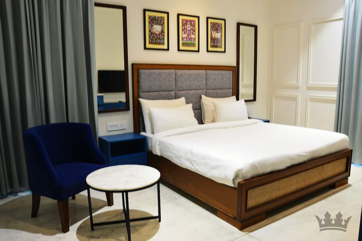 Een hotelkamer met een groot bed, een blauwe fauteuil, een klein rond tafeltje en een spiegel.