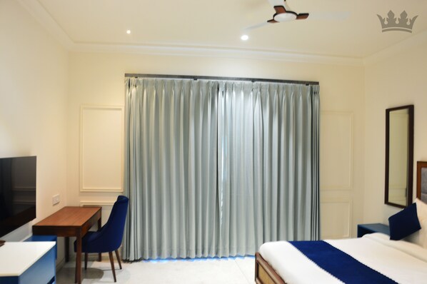 Habitación de hotel con cama, escritorio, silla, televisión y un amplio ventanal con cortinas.